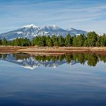 Snowcapped peaks in Arizona’s White Mountains reflected in a calm lake bordered by pine trees.